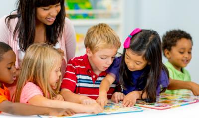 Five children and their teacher looking at picture books together.